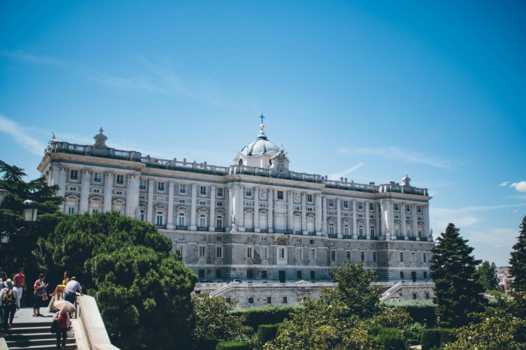 Stunning view of the Royal Palace of Madrid with surrounding greenery and tourists below.